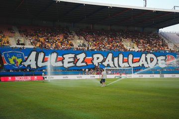 The images depict a lively soccer match at the Stade de la Mosson, featuring Montpellier HSC (MHSC) versus Rodez AF (RSFC) on the first day of Ligue 2, August 9, 2025, as indicated by the post text from Montpellier Ultras (@MHSC_ULTRAS). The first image shows a large banner reading "ALLEZ PAILLADE" with the MHSC logo, displayed by fans in the stands, with a player on the field and a crowd in the background. The second, third, and fourth images capture action near the goal, with players in orange and black kits (MHSC) and white kits (RSFC) engaged in play, a referee present, and enthusiastic fans waving a flag with red, black, and blue colors. The stadium is packed, with clear signage like "DÉPARTEMENT DE L’HÉRAULT" and "MONTPELLIER MÉDITERRANÉE MÉTROPOLE," reflecting a vibrant, supportive atmosphere. No platform watermarks are visible.