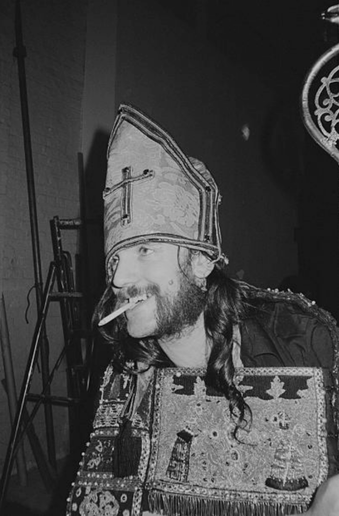 Lemmy Kilmister ( 1945-2015)...posed wearing a bishop's mitre hat & smoking  cigarette for 