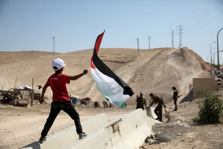 Today27News's tweet photo. A Palestinian Bedouin boy waves a Palestinian flag in front of Israeli soldiers at al-Khan al-Ahmar near Jericho in the occupied West Bank
#westbank_under_attack #UdeChile #Israel https://t.co/bzGeaBo3gG