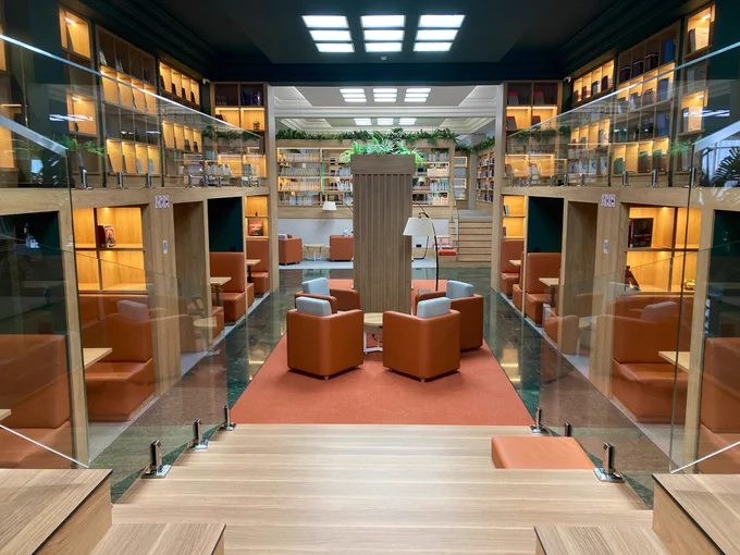 One of the reading rooms at MNU - it has a cuboid design featuring cosy soft furnishings and wooden shelving with glass panels. Yellow lighting is built into the shelves.