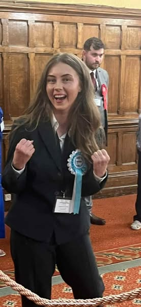 Reform Councillor Sienna Churcher jubilantly celebrating while the local MP’s son (Karl Scrogham) looks on solemnly.
