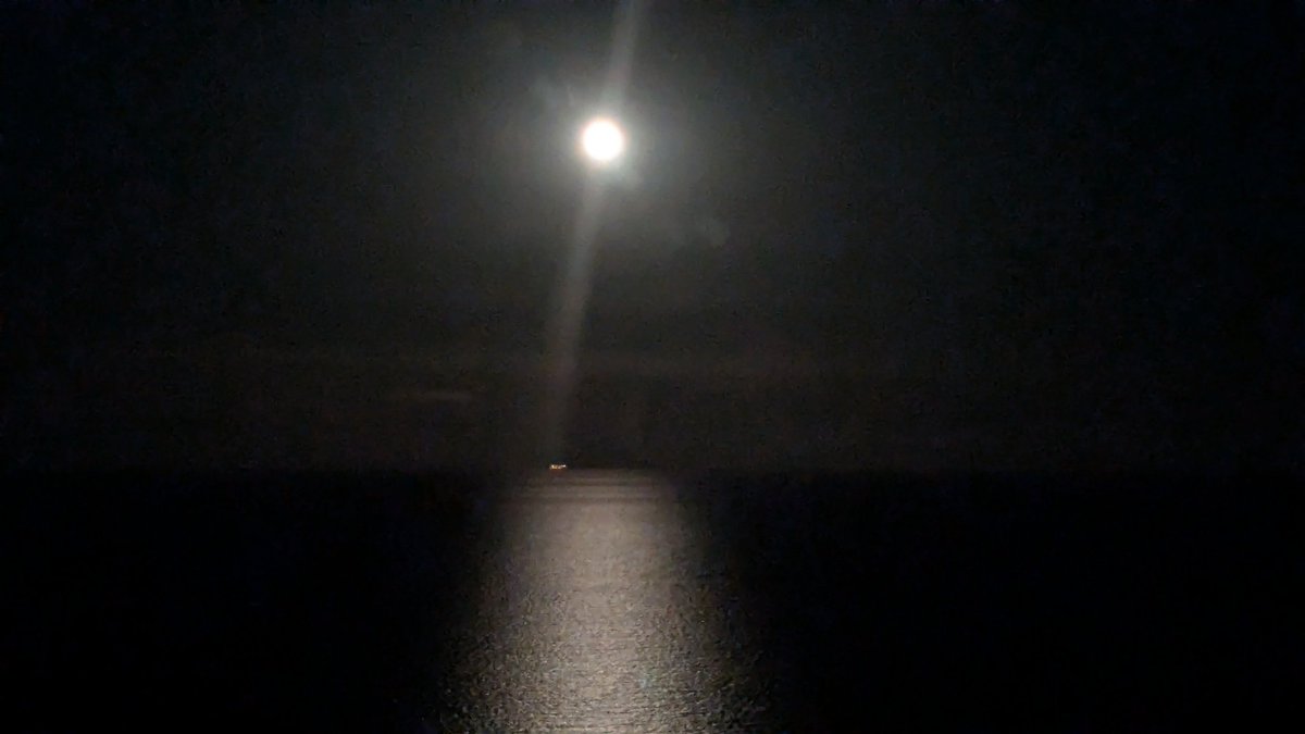 El placer de conducir de noche bajo la luz de la luna llena sobre el mar por la línea de costa.