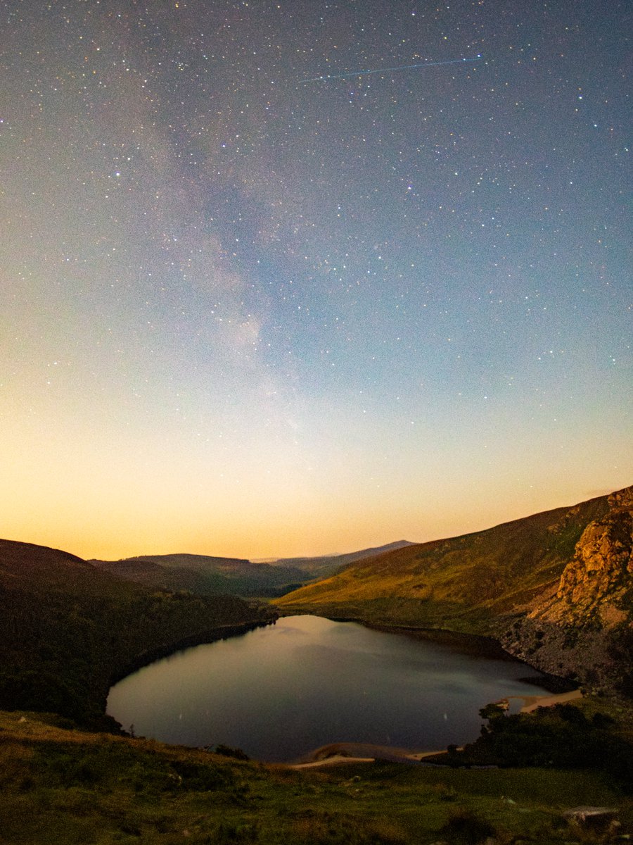 A warm night beneath the stars with a glimpse of the Milky Way setting in a hazy sky over Lough Tay.