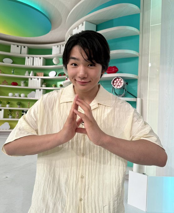 The image shows Kokoro Terada, a celebrity, standing indoors in a colorful, modern studio with shelves, plants, and vibrant lighting. He wears a light yellow short-sleeve shirt and has his hands clasped in front of him, smiling warmly. The background features a playful, artistic design with green and blue hues, suggesting a lively TV set. The post text from 日テレ公式 (@ntv_DayDay) indicates this is from the "DayDay." show, airing on August 14, featuring Terada as a weekday member, inviting viewer comments. No platform watermarks are visible.