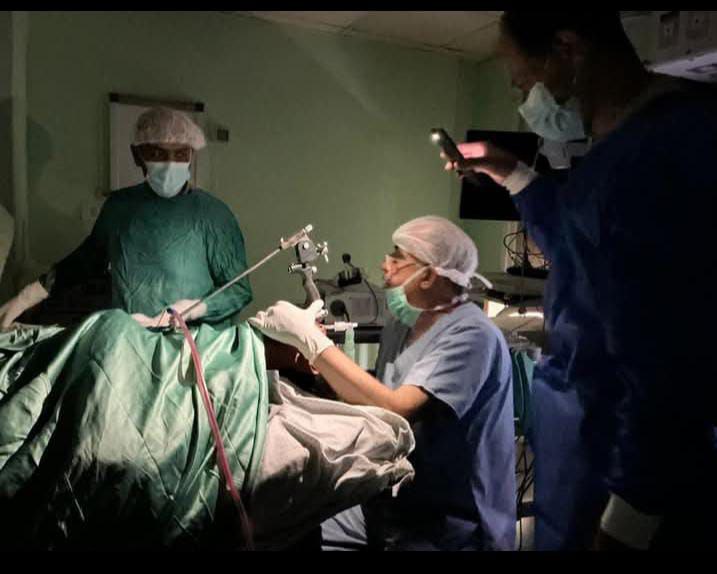 الدكتور أحمد الجدبة رئيس قسم الأنف والأذن والحنجرة في مجمع الشفاء بغزة يجري عملية جراحية لمصاب على إنارة كشافات الهواتف