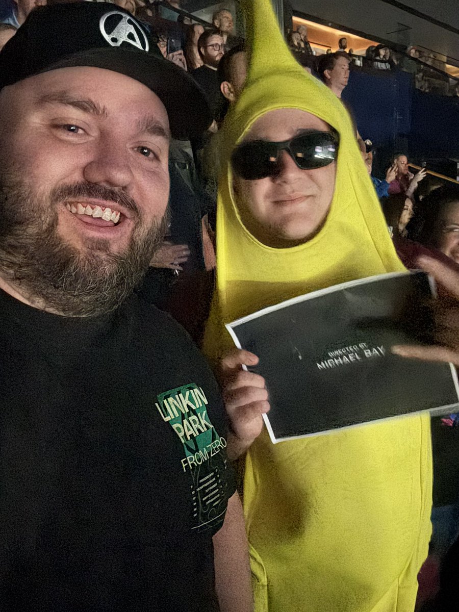 dhall_73's tweet photo. Linkin Park Live Review – Time Heals, Music Endures

For me, last night was a dream realized. I’ve always wanted to see Linkin Park live, but when Chester passed, I thought that dream was gone forever. Like so many fans, I couldn’t imagine how the band could go on. Then Emily came… not as a replacement (because Chester can never be replaced), but as someone who brought her own power, grit, and humanity.

When From Zero first released, I’ll admit I questioned the validity of the band continuing without Chester. At times it was hard not to feel like an imposter was behind the mic. But time heals, and I’ve grown to truly enjoy listening to From Zero. The band is leaning into Emily’s strengths and ability to move from polished vocals to raw screams. This created and creates music that both maintains and builds on Linkin Park’s authentic tone. Songs like Two Face felt like a continuation of Hybrid Theory, not an imitation.

Last night confirmed that for me. From start to finish, there was no sense of an outsider on stage. Emily doesn’t replace Chester… she belongs in Linkin Park! One of the most powerful moments was when she leaned over the rail separating fans from the stage, making herself visibly vulnerable, and showing the human connection that has always been the heartbeat of the band.

Lindsay Hall, who came mostly to support my love for the band, left captivated. She was blown away by Emily’s range, but also by the joy she saw on stage and in the crowd. Linkin Park clearly loves playing together, and their fans clearly love them right back.

The energy was unreal. A mosh pit and crowd surfing lasted for hours! This is something I’ve rarely seen feel that genuine and alive. And just to add to the surreal fun, I had the weird honor of standing next to a banana man holding a sign that read “Directed by Michael Bay.” It sparked laughs, and it helped Lindsay and others recall the Transformers connection to What I’ve Done, now trending again online.

And while last night was unforgettable, I also want to say this: Linkin Park has always spoken to adult thoughts and emotions such as loss, anger, resilience, and healing. That’s part of what makes their music so powerful, but it also means the themes and language aren’t really suited for young kids. Their shows are raw, honest, and human which is exactly why they connect so deeply with the people who need it.

Verdict: Chester can never be replaced. But Emily has proven she cannot be either. Linkin Park has found a new normal that is rooted in respect, joy, intensity, and connection. Last night wasn’t just a concert; it was living proof that Linkin Park is still authentically Linkin Park.
#fromzeroworldtour #LinkinParkNashville #LinkinPark
