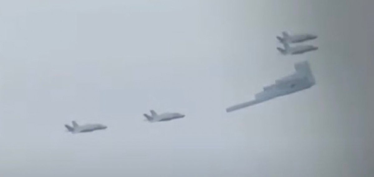 sentdefender's tweet image. A U.S. Air Force B-2A “Spirit” Long-Range Strategic Stealth Bomber escorted by 4 F-35 Lightning IIs passes over as President Donald J. Trump and Russian President Vladimir Putin meet and shake hands at Joint Base Elmendorf–Richardson in Anchorage, Alaska.