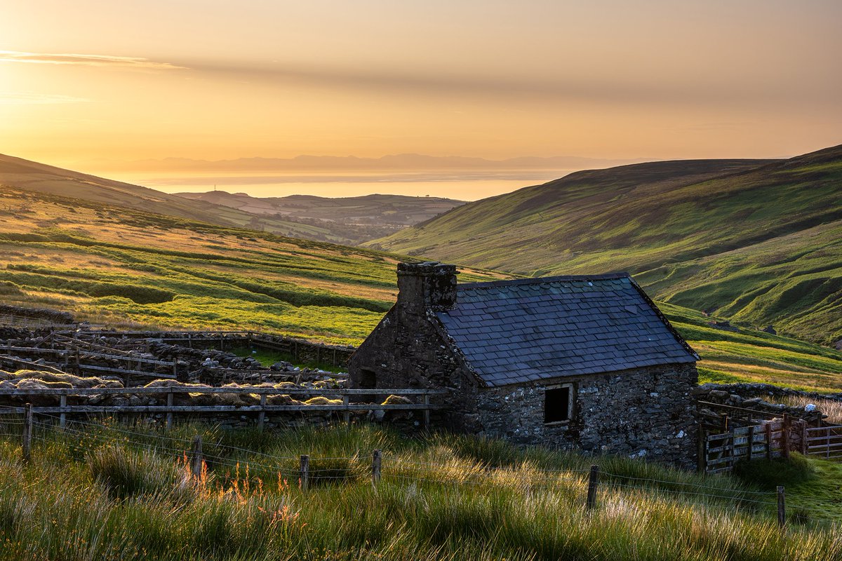 The shepherds hut at the top of the Corrany Valley captured as the early morning summer sunlight floods into the scene. A thin strand of cloud out to the east blocks the bright sunshine and casts a strange eerie shadow across the entire sky #iom #isleofman #landscapephotography
