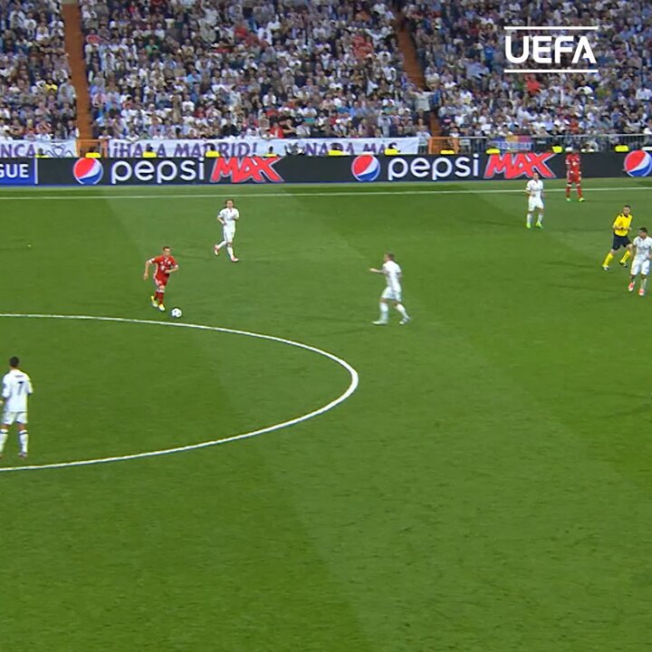 A soccer match in progress at a stadium, with a player in a red jersey advancing with the ball near the center circle while opposing players in white jerseys and a referee in yellow look on, featuring "UEFA," "Pepsi Max," and "Hala Madrid" signage along the sidelines. The image appears to capture a moment from a UEFA Champions League match, likely featuring Real Madrid, fitting the context of a notable goal scored by a young player against Bayern Munich.
