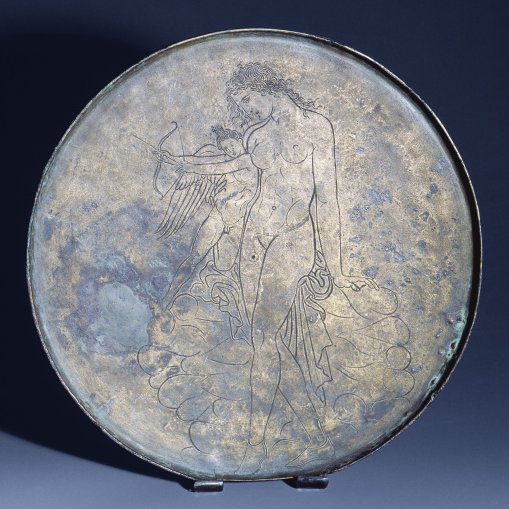 Aphrodite leaning on a rock and guiding the young Eros as he learns to draw the bow. Bronze mirror cover, (c. 350 BC)