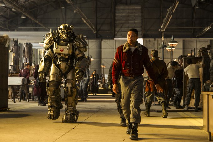 Maximus walking in a Brotherhood of Steel base in Fallout Season 2. He has a new red jacket we haven’t seen yet. There’s someone in Power Armor behind him to his right