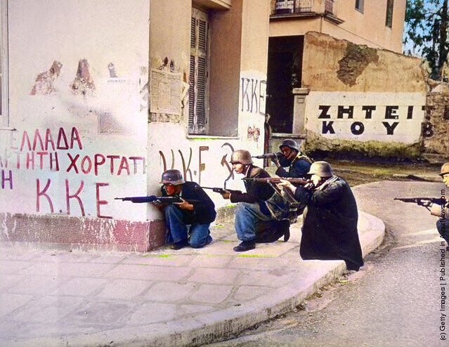 The Greek People's Liberation Army engaged in a street battle in Athens with the British . December 1944. They are using captured German helmets and Italian rifles . You can also see the K.K.E communist party of Greece graffiti on the wall .