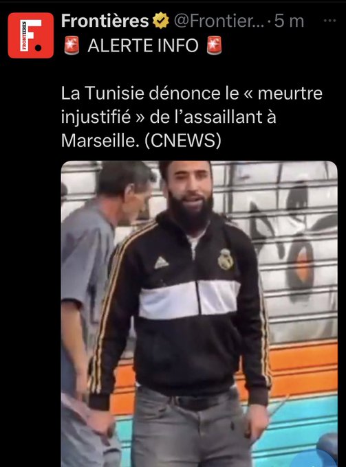 A man wearing a black and white Adidas jacket with yellow stripes, standing outdoors near a colorful graffiti wall. Another man in a gray shirt is visible in the background. The text overlay on the image reads "ALERTE INFO" with red star emojis and mentions Tunisia and Marseille.