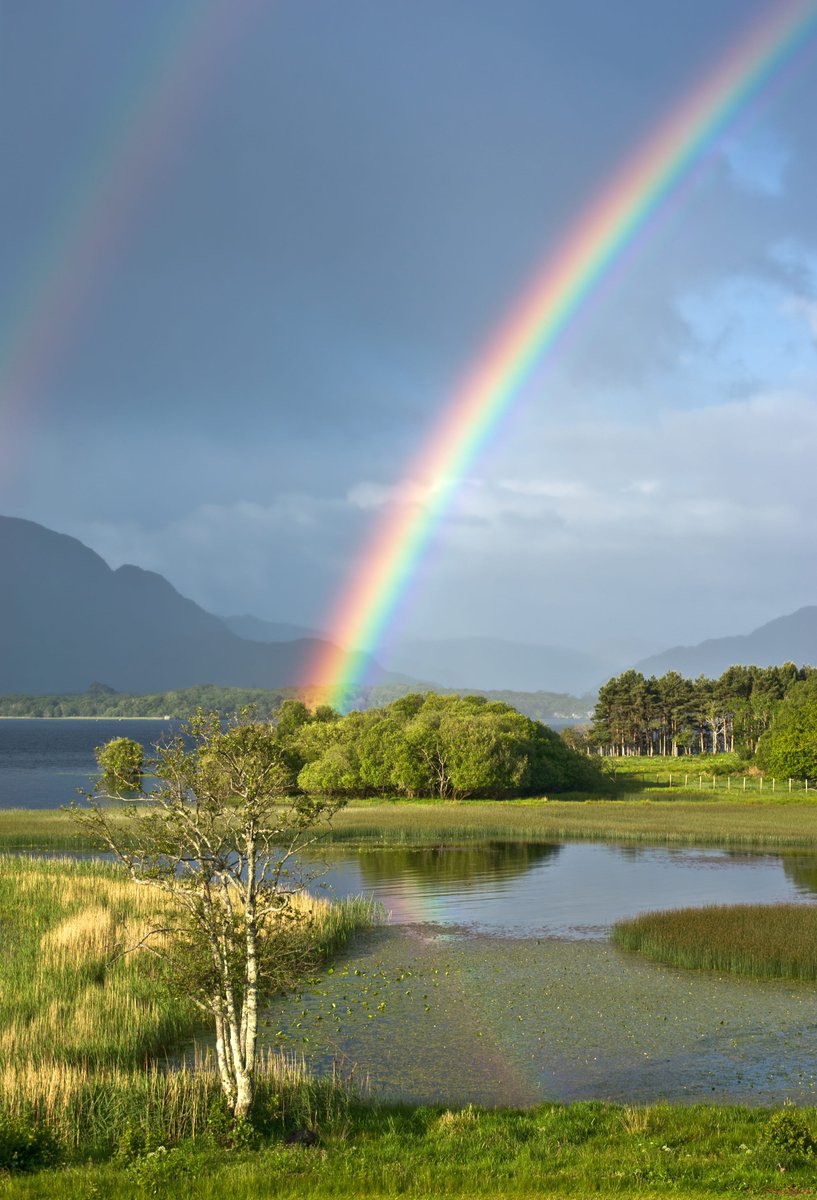 A genuine Irish double rainbow is reflected in the waters of Lough Leane, Killarney, Ireland, with the misty Kerry mountains in the background.