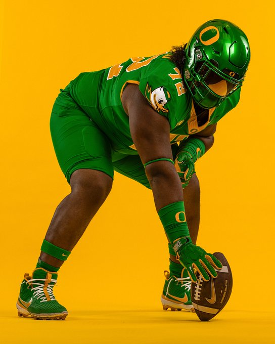 A football player wearing a green and yellow Oregon Ducks uniform, number 72, with "Laulotu" on the back. The player is in a crouched stance, holding a football, with green gloves, wristbands, and cleats. The uniform features the Oregon Ducks logo and Big Ten Conference patch.