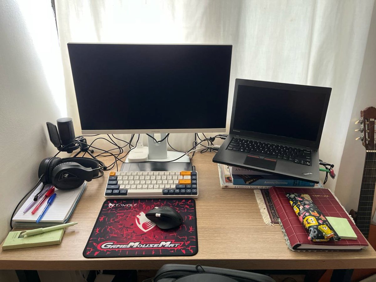 ablzh_dev's tweet image. Here’s my current desk: external monitor + ThinkPad propped on a few books, mech keyboard, big mouse mat, headphones, and a guitar peeking in. What does your setup look like? Reply with a photo 👇 #DeskSetup #WFH