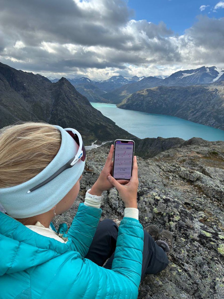 Person holding phone running Celestia light node on a mountain overlooking a turquoise lake in Norway