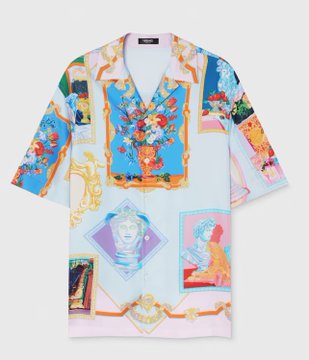 Shows Pietro Schirano wearing a colorful Versace shirt with AI clothing change effect, featuring floral and classical art patterns, with tropical beach resort background