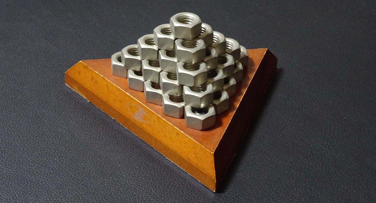 ナットを２個・３個・４個・５個でつくった10個のピースを組み合わせてピラミッドをつくるパズル。整った形のピラミッドを完成させるために木製の土台が準備されている。最後のピースを組み合わせるときには少し不安になる。シールは取れてしまっているが(株)河田が大人向けのパズルとして販売した。