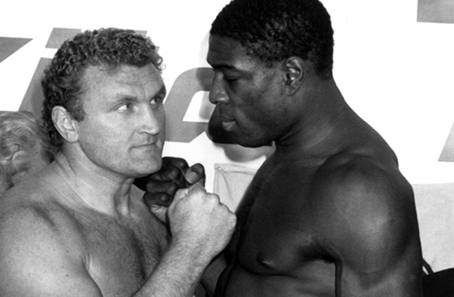 A poster for a boxing match between Frank Bruno and Joe Bugner, showing both men in boxing gloves and stance, facing each other. Smaller inset photos of their faces are visible. Text on the poster reads "The Last Word is . . . GOODBYE! FRANK BRUNO (England) Vs JOE BUGNER (Australia)" and includes details about the event date, location, and supporting bouts. A black-and-white photo of Frank Bruno and Joe Bugner standing close, fists raised, during a face-off.
