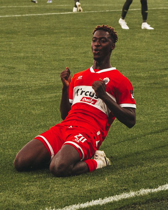 Mohamedou Doumbia kneeling on a grassy soccer field, wearing a red jersey with 