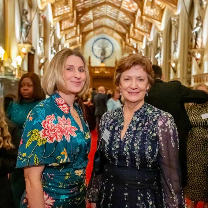 Caitlin Harvey and Helene Buijs standing beside each other at the Carer’s Reception at Windsor Castle. Caitlin is smiling, she has bob length blonde hair and is wearing a floral teal dress. Helene has short brunette hair and is wearing a navy blue dress with a floral pattern. They’re both smiling at the camera.