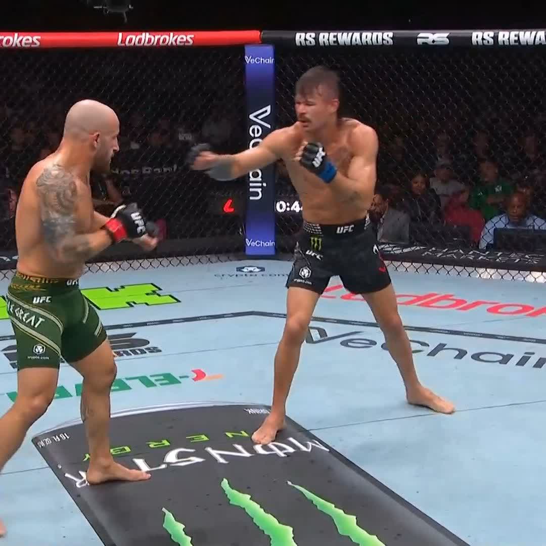 Two UFC fighters in an octagon during a bout, with one fighter throwing a punch at his opponent; sponsorship logos including Ladbrokes, VeChain, Monster Energy, and crypto.com are visible.