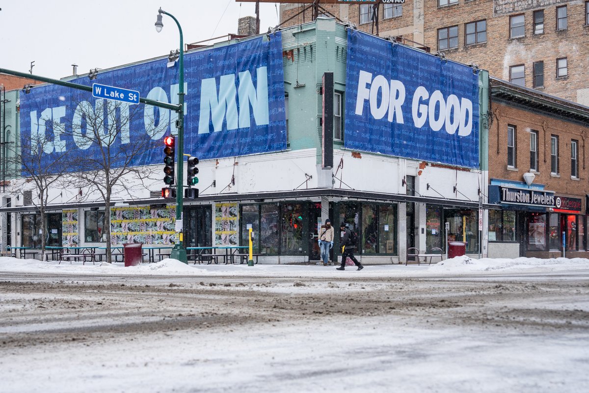 Large banner hangs over a building at Lake Street and Lyndale Avenue on a snowy morning. 

It reads "ICE OUT OF MN" "FOR GOOD" with the names of those killed by federal agents.

Minneapolis, February 2026