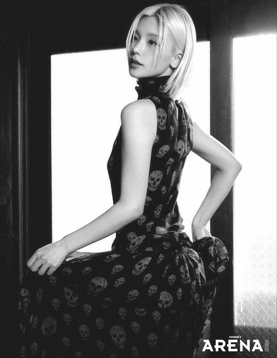 Black fabric marked with red skulls sways softly against warm wooden walls, bold in print yet oddly relaxed in presence. One hand gathers the dress, the other lets the moment stretch, because sometimes styling works best when it pretends not to care