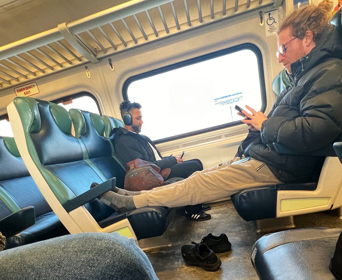 Bro is yapping on his phone, shoes off, feet up. The man bun is really the cherry on top. #LIRR