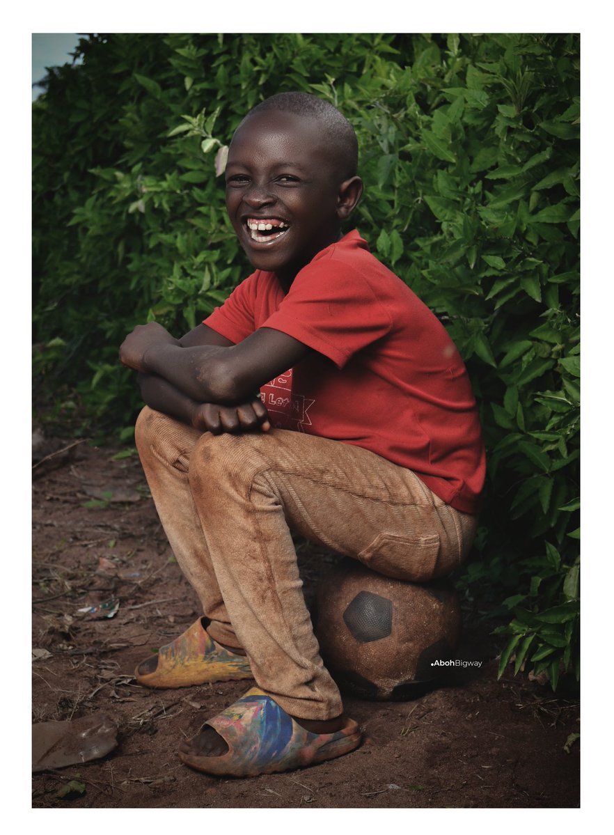 He sat on an old football like a throne, laughing at a world that hadn’t taught him worry yet. 
The ball was worn, the ground dusty, but joy needed nothing new. In that moment, with green leaves behind him and laughter ahead, life was simple and enough.
