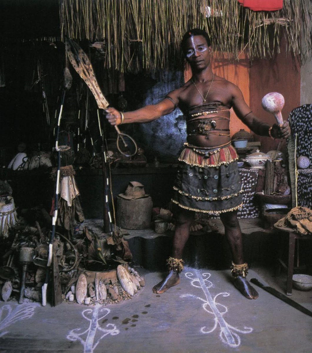 Chief priest Úyìèkpèn, priest 'Ọbọ' of Ògún, the god of metal, toolmaking, and weapon. The ferocious god of war, in front of his ogun shrine holding the edo eben scepter and a guord,ca.1994.