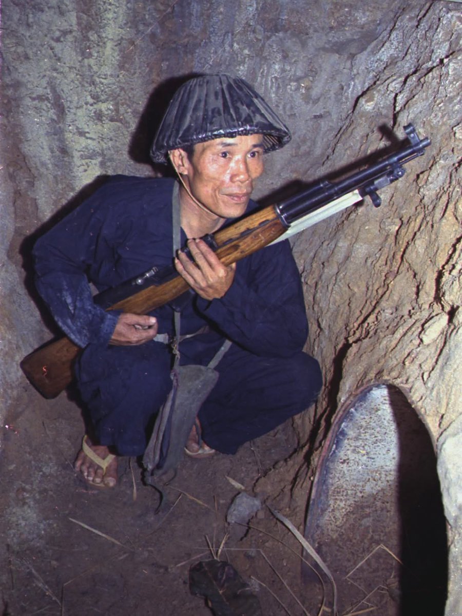 A guerrilla fighter from the Popular Armed Forces of Liberation, armed with a Soviet SKS rifle, crouches in a tunnel waiting to ambush U.S. invaders. Vietnam, 1968.