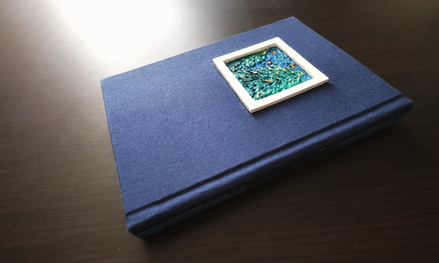 a_ryu_dot's tweet photo. 手製本作品2025年度『1/28』
 昨年に続き長編小説一話を一冊の手製本に綴じていきます。
一冊目は窓つきの糸かがり。
主人公たちが窓（木枠）から覗き込みみつめる絵の一枚をテクスチャーアートで描きました。
表紙を凹ませ、木枠は飛び出させています。
背から糸が見えるかたちで夜の紺色を集めました https://t.co/iDQOsnITUJ