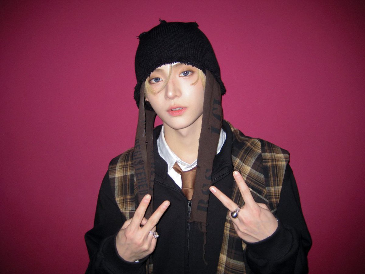 ᅠ
Against a fuchsia blaze, he stands in shadowed plaid and sable knit—golden fringe grazing porcelain calm. Twin peace signs glint with silver rings, a quiet rebel wrapped in sepia checks and midnight cool.
ᅠ