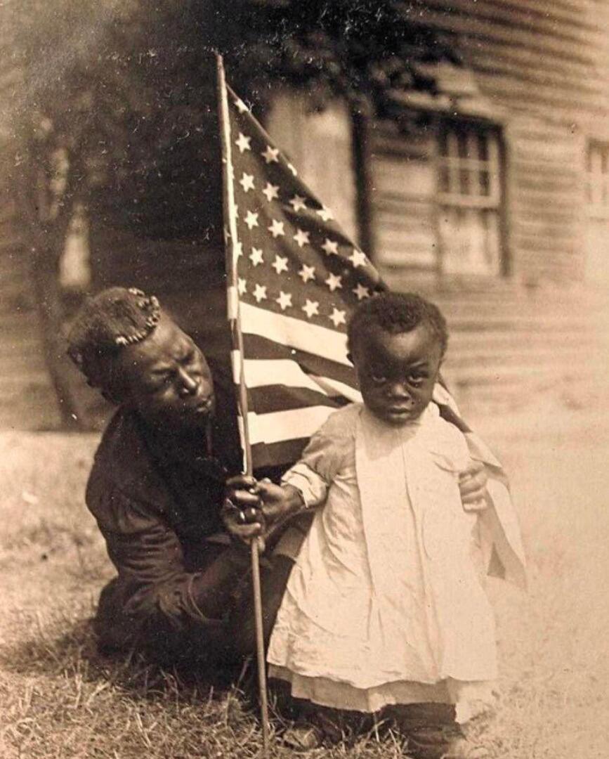 An American mother and daughter hold the American flag in the early 1900s.