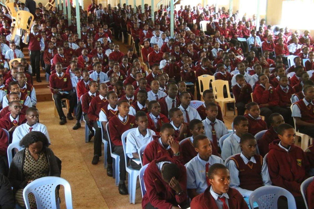 Large group of uniformed students seated in assembly hall listening