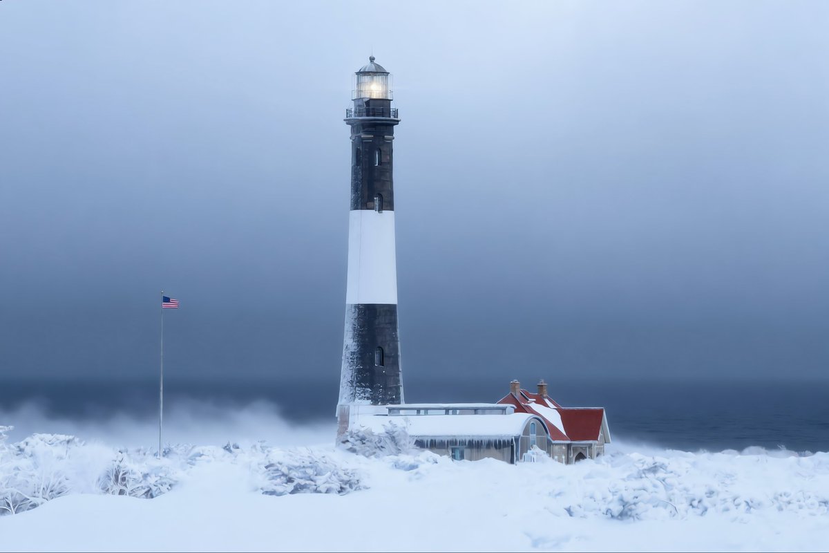 Fire Island Lighthouse stands tall in a whiteout, the coast swallowed by wind carved snow. The keeper’s house is iced and frosted, the Atlantic churning dark behind it. Red roof. Black tower. Endless white.

When winter roars, the beacon does not blink. It simply keeps shining.