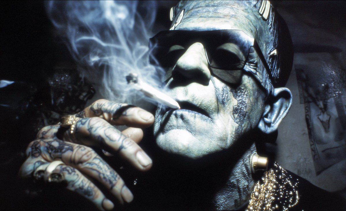 Love this prompt Brian. close-up of Frankenstein in black sunglasses,  smoking marijuana with smoke coming out of his mouth, wearing a black and  gold beaded shirt, with tattooed hands, shot on kodak