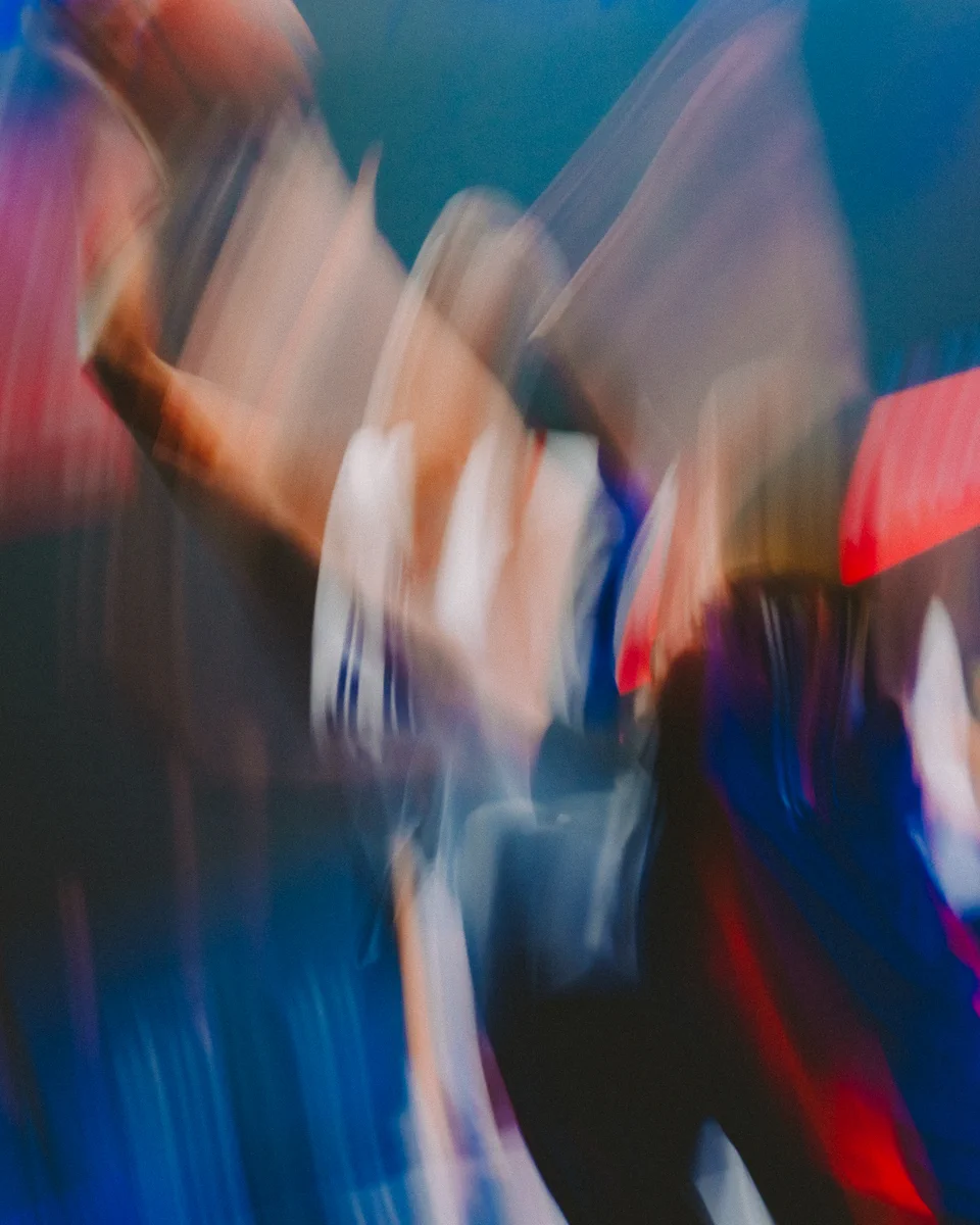 Motion blur abstract of a figure in what appears to be a uniform, with blues, reds, and whites dominant. The movement implies action, possibly sports-related.
