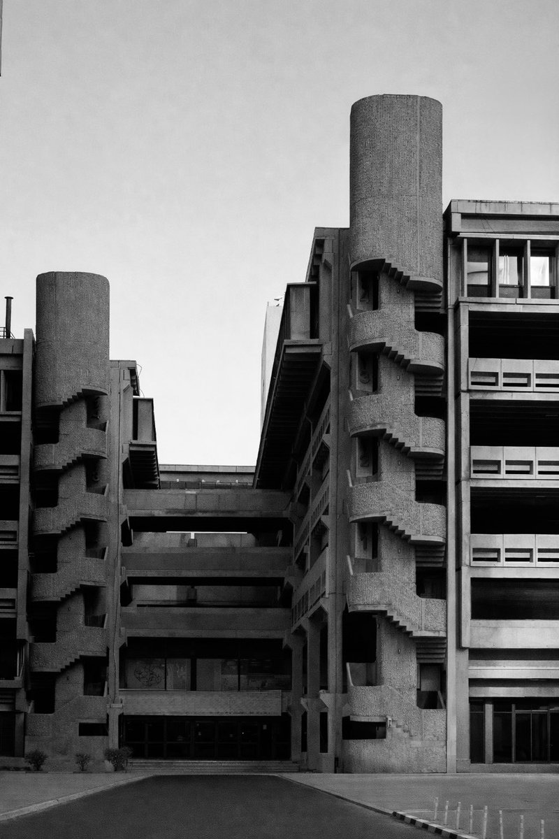 في قلب مدينة الكويت، تقف هذه البناية كواحدة من الشواهد الصامتة على مرحلة معمارية قصيرة لكنها مؤثرة: مرحلة العمارة الوحشية (Brutalism) التي مرّت على الكويت في سبعينيات وثمانينيات القرن العشرين.
الواجهة الخرسانية الخشنة، والسلالم الحلزونية الخارجية، والأبراج الأسطوانية المتصلة