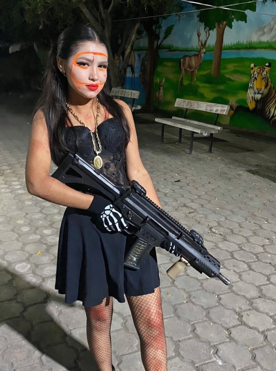 The daughter of a CJNG member affiliated with the "Guerreros" faction, seen here armed with a CX-05 carbine (a compact/short-barreled variant of Mexico's FX-05 Xiuhcoatl rifle). The weapon is set up with a straight/vertical front grip and MBUS-style flip-up iron sights.  Where