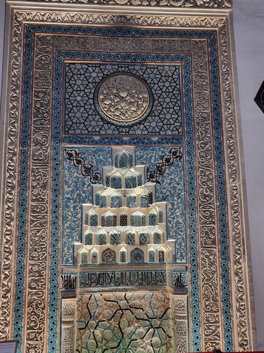 ECNHLC's tweet photo. Selçuklu'nun şaheseri ahsap sütunlu ender camilerimizden Aslanhane caminin mihrabinda bulunan  yuvarlak, gül görünümlü kabartma aslında hayat ağacının tepeden görünüşü veya çekirdeği/meyvesi olarak yorumlanıyor. Orta Asya’dan Anadolu’ya taşınan bu sembol, zamanla İslam sanatında doğrudan bir ağaç figüründen ziyade, merkezden çevreye yayılan dairesel bir "şemse" (güneş/çiçek) formuna dönüşmüş.
​Tasavvufi mimaride Hayat Ağacı, kökleri gökte, dalları yerde olan ve meyveleriyle inananları besleyen Cennet’i simgeler.
Namaz kılan kişinin tam karşısında durması, ibadet anında kişinin yöneldiği yerin aslında "sonsuzluk ve cennet" olduğu mesajını verir.
​Hayat ağacının gövdesi tektir ama dalları (kesret) çoktur. O dairesel kabartma, tüm dalların birleştiği o kutsal merkezi, yani Allah’ın birliğini (Tevhid) temsil eder. Dışa doğru açılan yapraklar ise bu tek kaynaktan yayılan yaratılışı sembolize eder.
​Eski Türk kültüründeki "Dünya Ağacı" (Kayı), İslamiyet ile birlikte cami süslemelerinde geometrik bir disiplinle yeniden yorumlanmıştır. Ankara’daki Ahilik dönemi eserlerinde bu geçişin izlerini; bitkisel motiflerin geometrik formlara (daire, yıldız) hapsolmuş haliyle sıkça görürüz.
​Özetle bu gül motifi, Hayat Ağacı’nın bir mikrokozmosu (küçük bir özeti) gibidir. Hem Hz. Peygamber’i (gül sembolü üzerinden) hem de ebedi hayatı ve ilahi nizamı (hayat ağacı üzerinden) aynı anda simgeliyor.