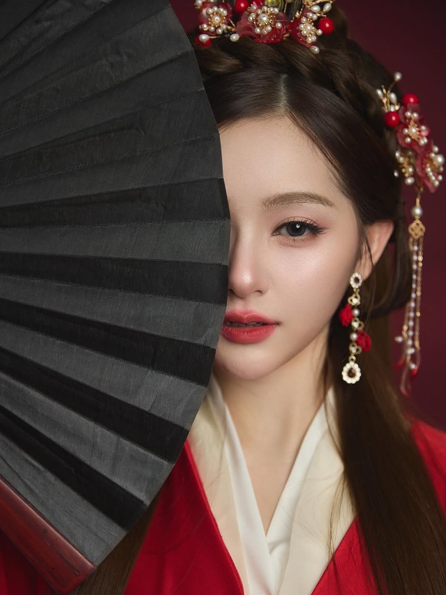 mimrts's tweet photo. Silk whispers across quiet shoulders while crimson folds cradle a softened heartbeat. Behind the fan, a gaze lingers like a secret waiting for dusk. Each ornament trembles with delicate stories, swaying between grace and restraint. https://t.co/YZN9HmQxH0