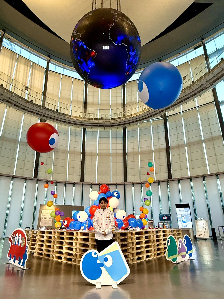 大屋根リングを想起させる展示台。
そこに広がる、万博民による2次創作。

そこから――
上空へ舞い上がる「こみゃくたち」。
視線の先には、未来館の象徴・ジオ・コスモス🌏

その周囲を取り囲むのは、
まるでパビリオンのように点在する展示群。

さらに上空には、
