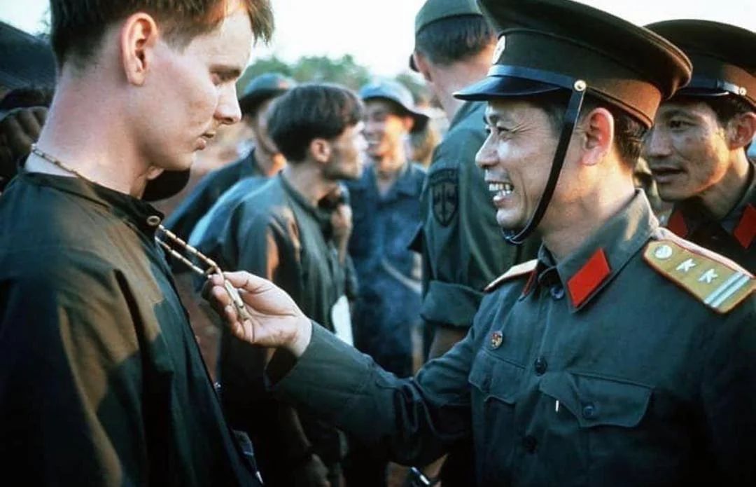 A North Vietnamese Army officer laughs at the peace symbol necklace of a captured American soldier, North Vietnam, 1973.