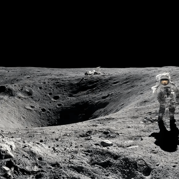 This imag captures a moment during the Apollo 16 mission in April 1972, showing the lunar surface.
The astronaut in the foreground is standing near Plum Crater, which was visited during the mission's first extravehicular activity. In the background, the Lunar Roving Vehicle (LRV)