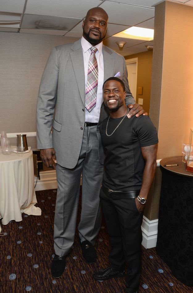 NBA legend Shaquille O'Neal and comedian Kevin Hart pose for a photo at a formal event, showcasing their famous height difference in an indoor setting.