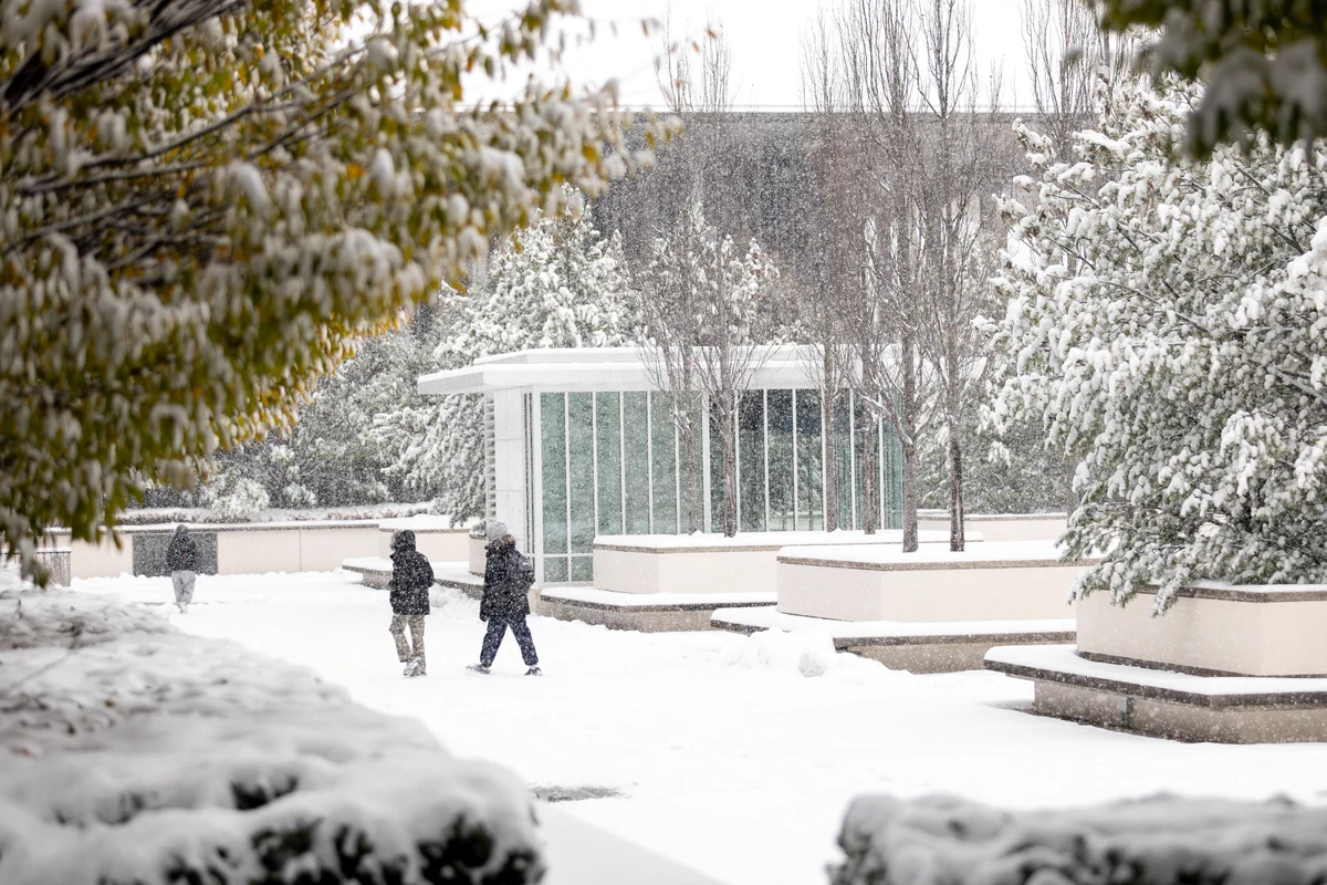 Three people seen walking across the UAlbany podium during a snow storm. 