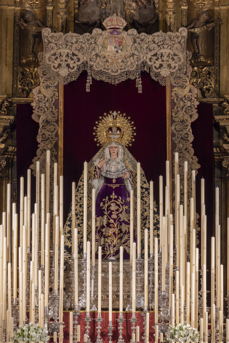 SEPTENARIO | El altar se dispone con varias alturas a modo de gradas cuajadas de candelería, donde destaca la presencia de un alto dosel realizado ex profeso con los respiraderos laterales del paso de palio y la bambalina frontal realizada por Victoria Caro en 1942. Bajo este se